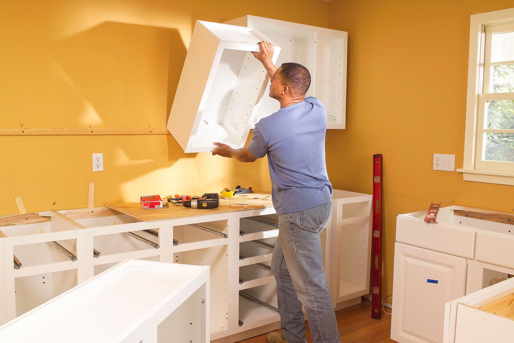 Professional handyman in work uniform installing cabinet in kitchen